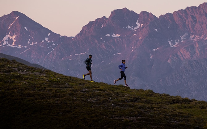 Two runners going downhill with peaks in the distance